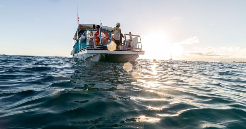 Sunlit passenger boat floating on sparkling ocean at sunset, people on deck enjoying a coastal boat tour