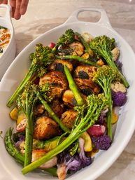 Oval white serving dish of seared scallops glazed in sauce with roasted seasonal vegetables — broccolini, asparagus, purple cauliflower and radishes.