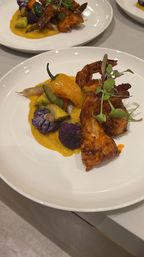 Grilled shrimp curled over bright butternut squash puree with purple cauliflower, roasted yellow pepper, mixed vegetables and microgreens on a white plate — colorful seafood fine-dining dish.