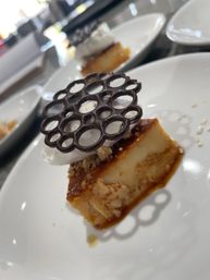 Caramel flan slice topped with whipped cream, crunchy crumble and a decorative chocolate lattice on a white plate — plated gourmet dessert.