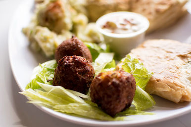 Crispy golden fritters on crisp lettuce with dipping sauce, potato salad and flaky pastry on a white plate.