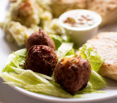 Crispy golden fritters on crisp lettuce with dipping sauce, potato salad and flaky pastry on a white plate.