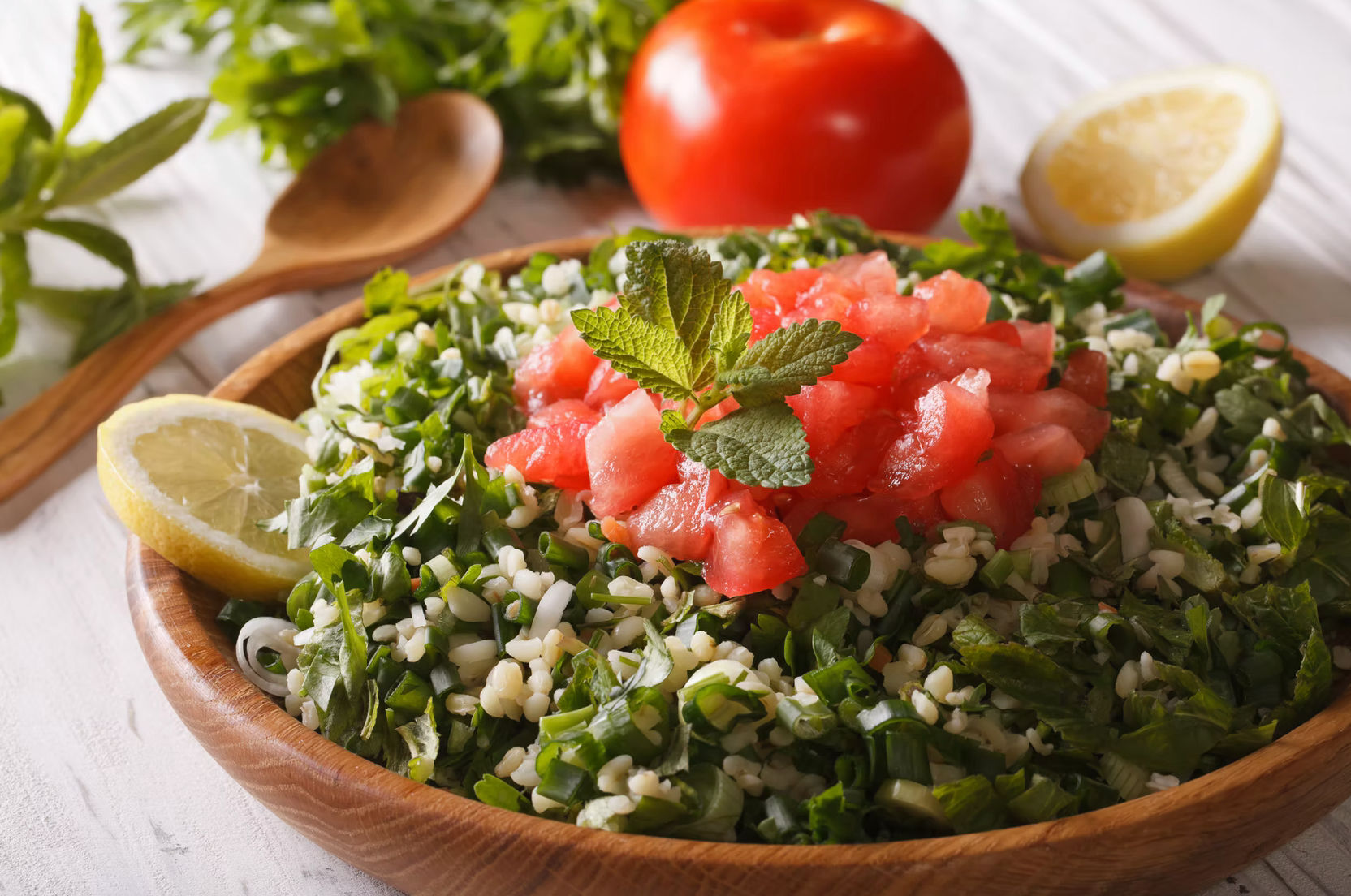 Zesty Mediterranean tabbouleh in a wooden bowl with chopped parsley, bulgur, green onions, diced tomatoes, fresh mint and lemon wedges